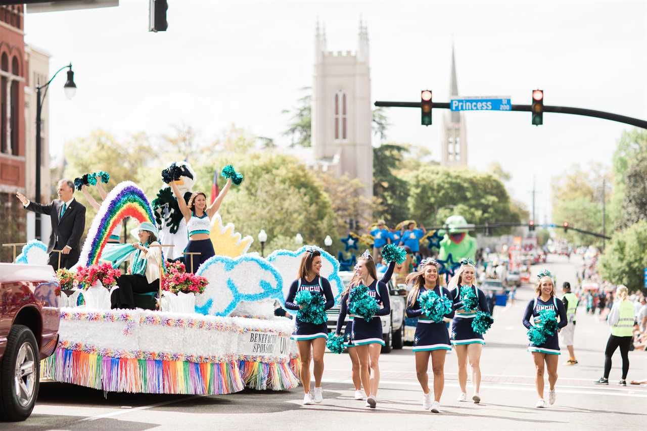 Cheerleaders walk alongside a colorful float carrying dignitaries.