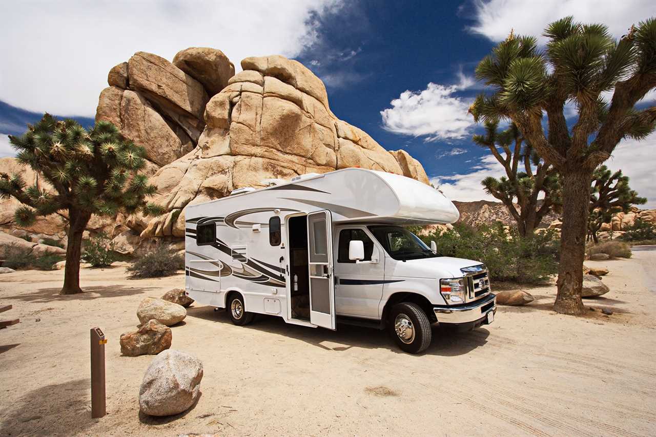 RV parked near boulders between two Joshua trees.