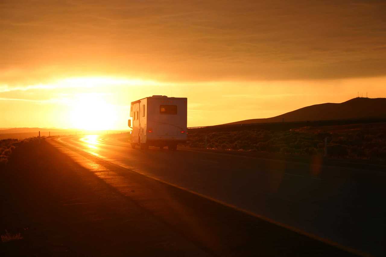 An RV drives toward an orange sunset.