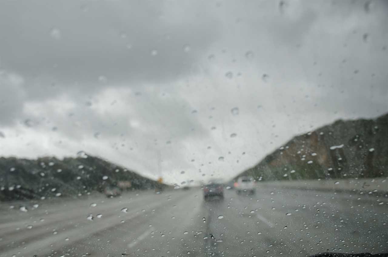 Cars driving on the freeway on a mountainous pass in rainy weather.