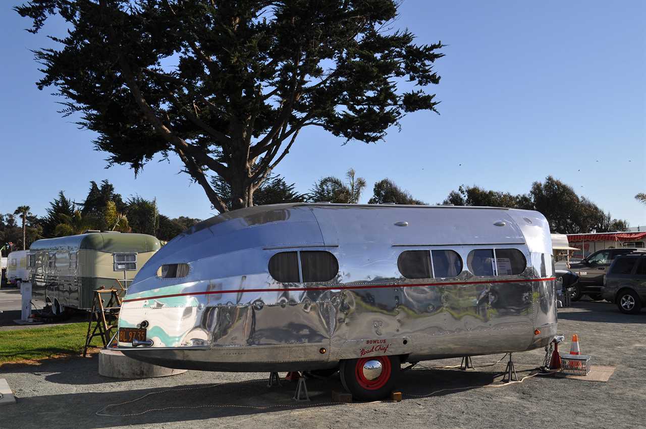 Vintage 1930s Silver bullet trailer parked near fir tree.