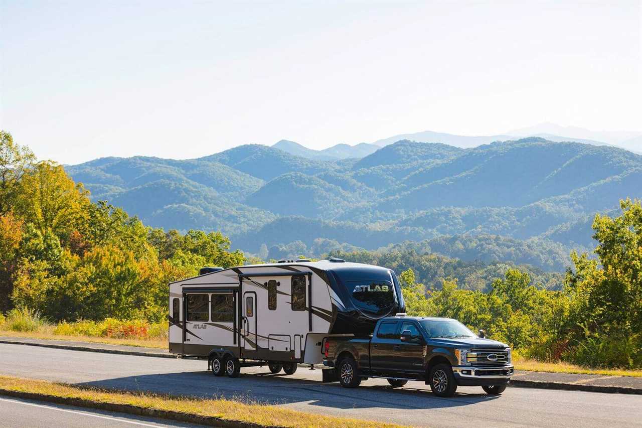 A truck pulling a fifth-wheel motoring down a highway with mountains in the background