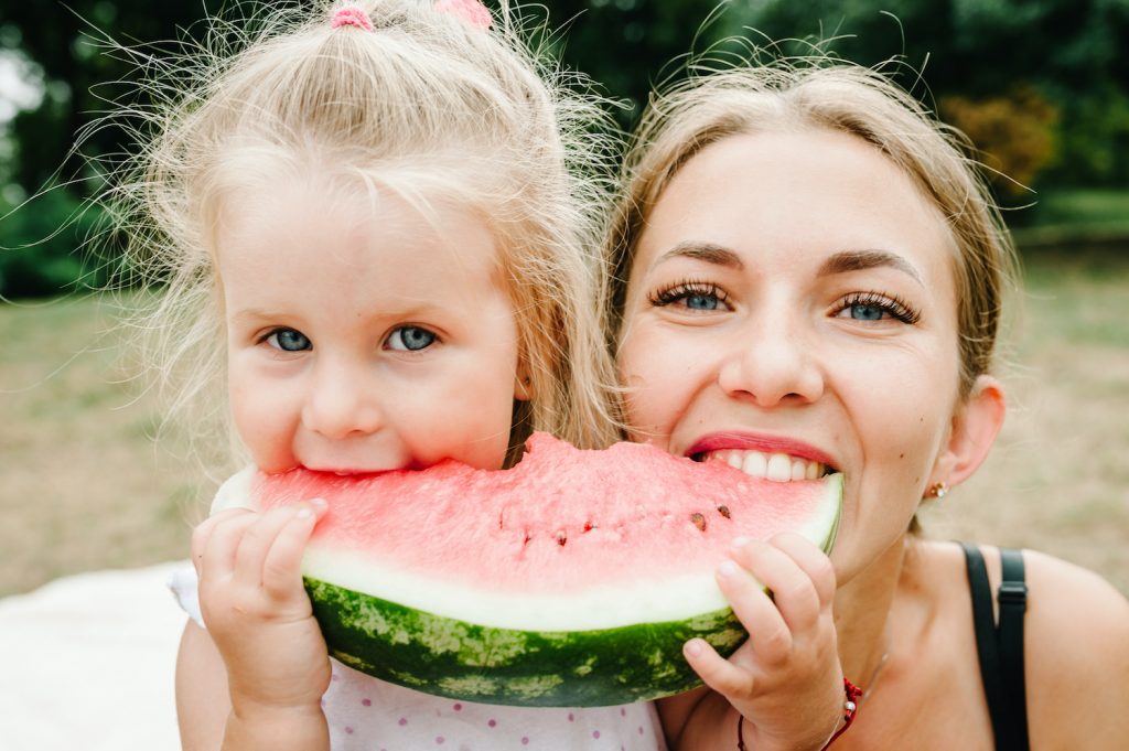 Cute daughter with mother eating watermelon in the summer. Happy girls in the park.