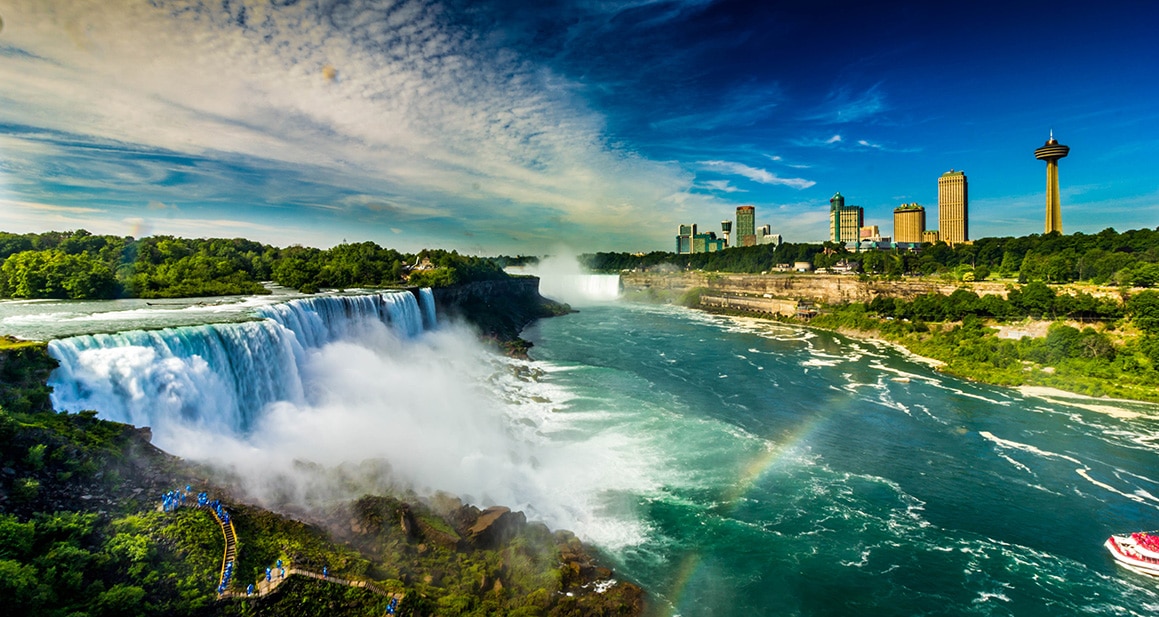 Waterfall roars as buildings loom on the horizon.