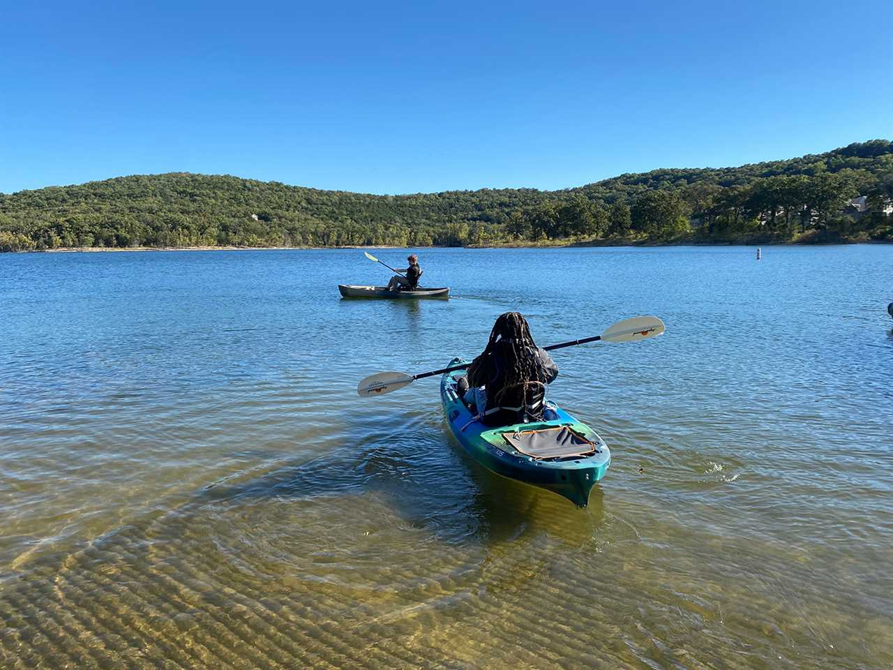 Kid with red hair and man with dreadlocks kayak on tranquil waters.