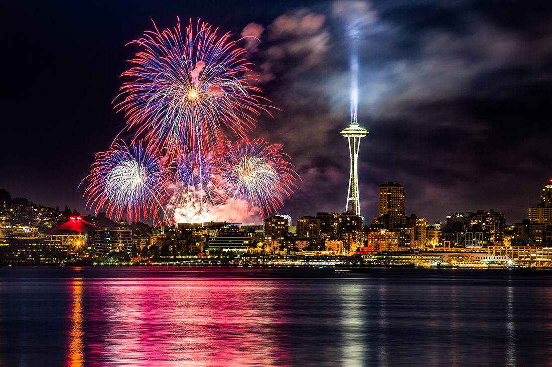 A fireworks display amid a cityscape reflected on the water.