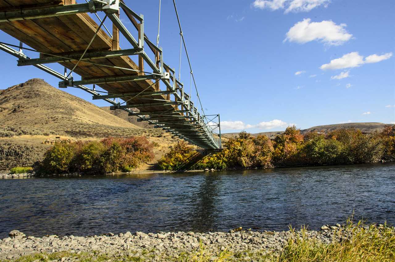 Narrow Footbridge spans a river in an arid landscape.