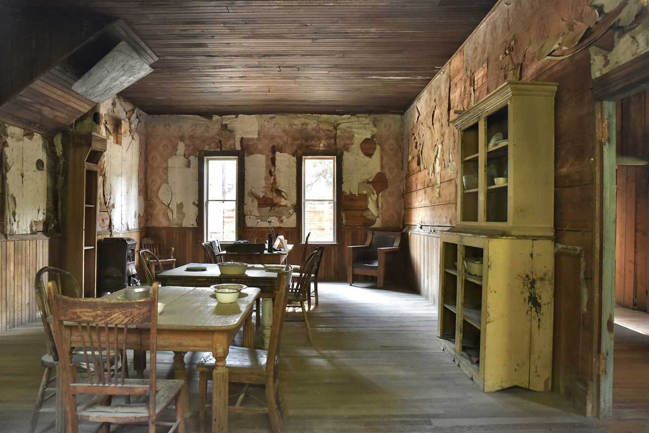 A room in an 1800s design with chairs, tables and a cupboard with empty shelves.