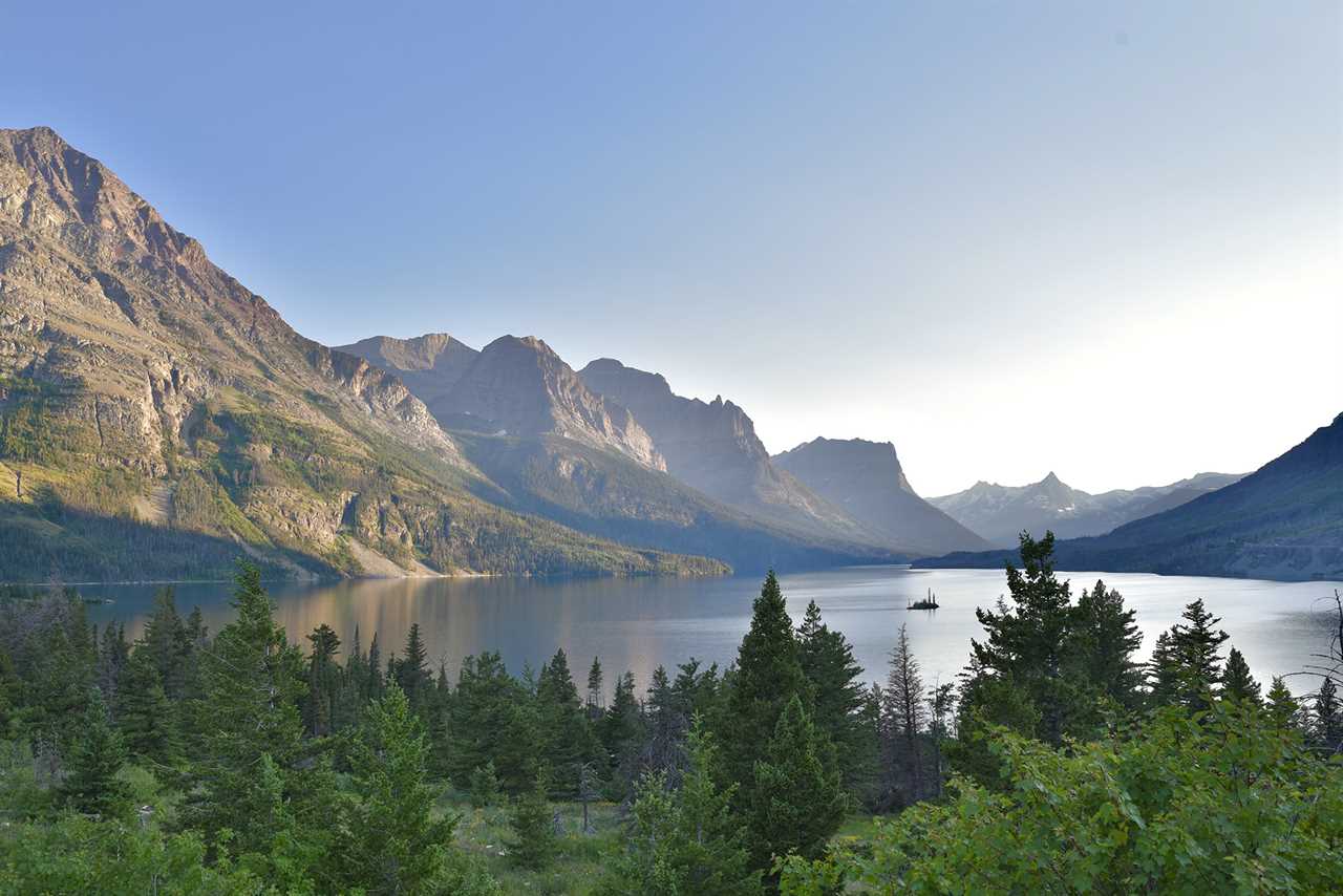 A vast, serene lake with a tiny island flanked by towering peaks.