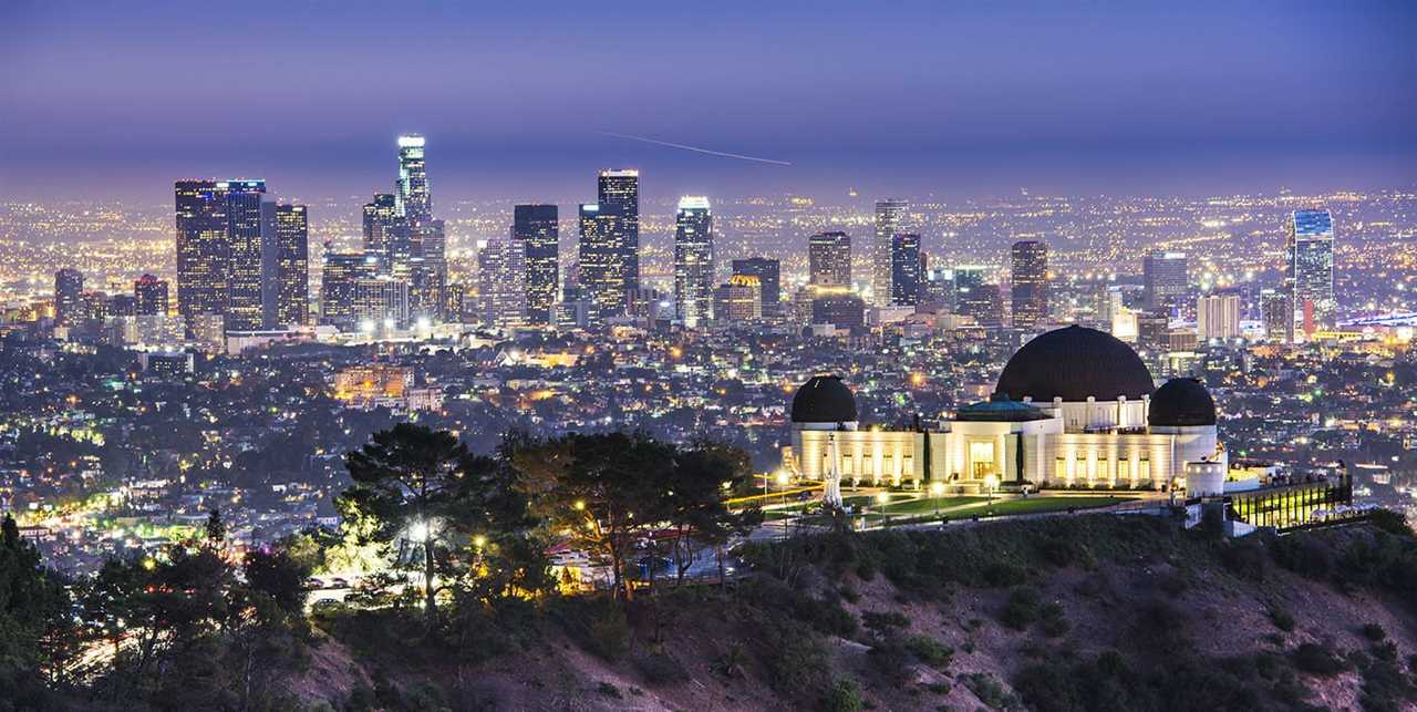 An observatory sits on a bluff while towering skyscrapers loom in the background.