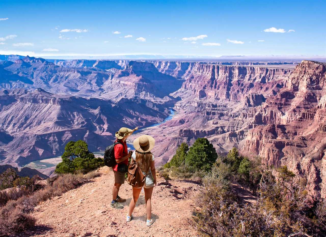 Couple on top of the mountain, looking at beautiful summer mountain landscape. Friends on hiking trip enjoying view of Colorado river. South Rim. Grand Canyon National Park, Arizona, USA.