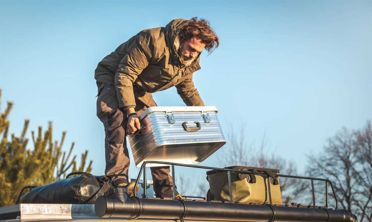 A man is lifting a metal box on the roof of a camper van surrounded by nature