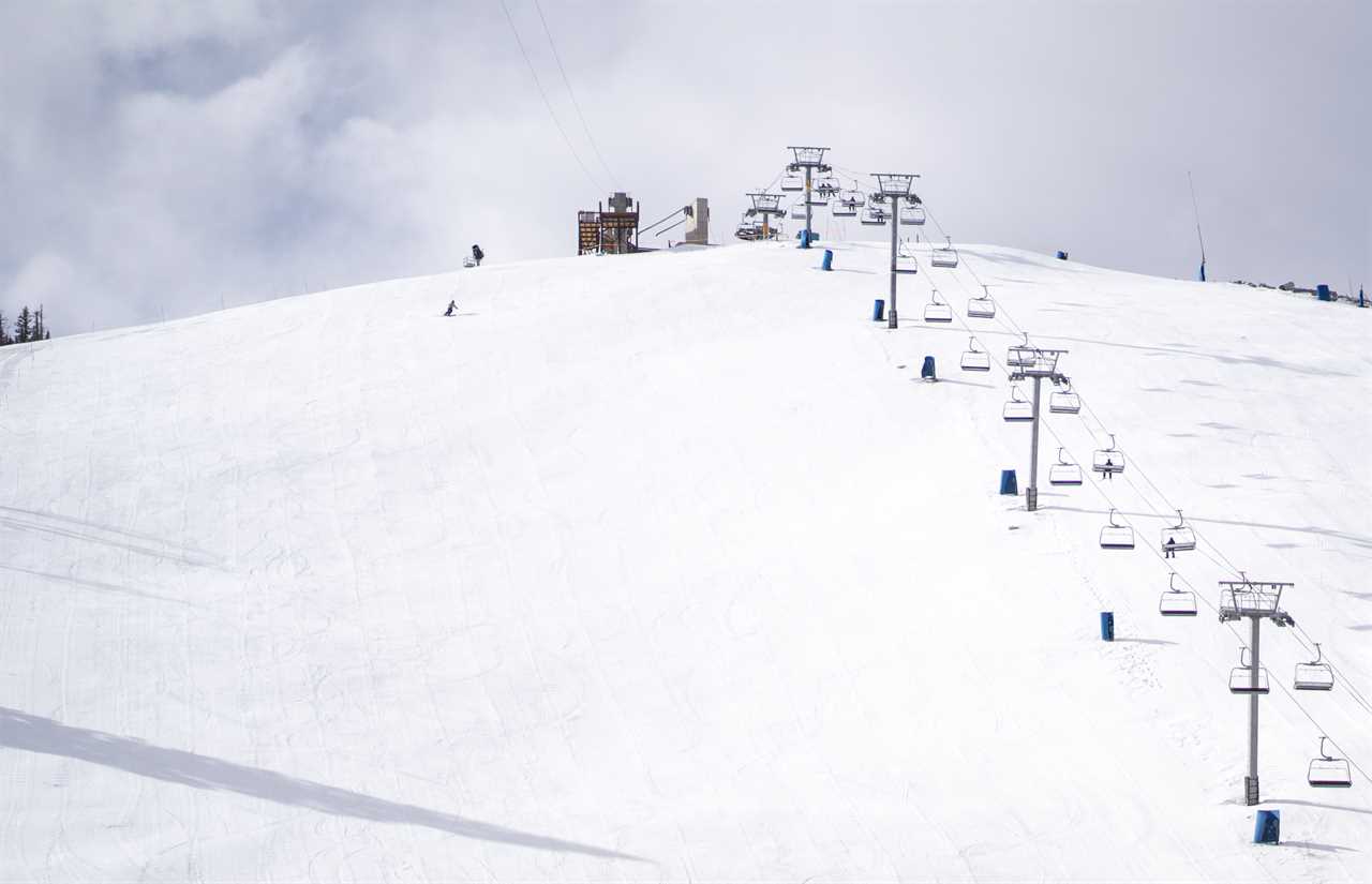 A ski lift carries skiers ove a snow-covered hill.