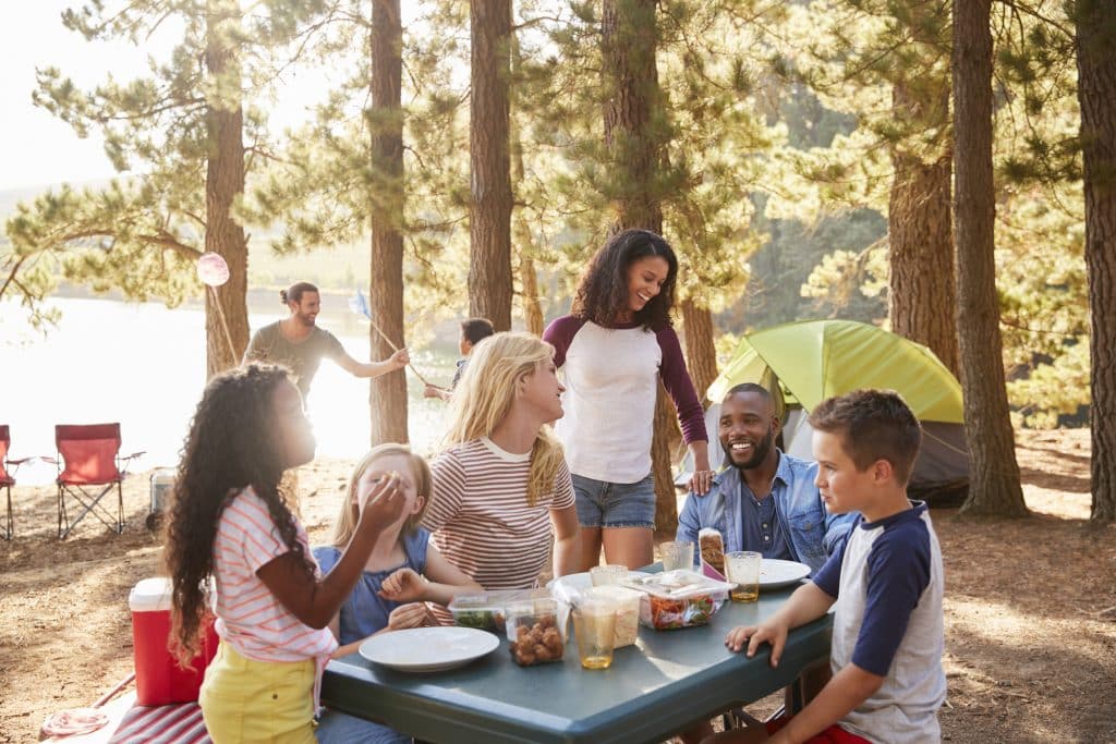 Family With Friends Camp By Lake On Hiking Adventure In Forest