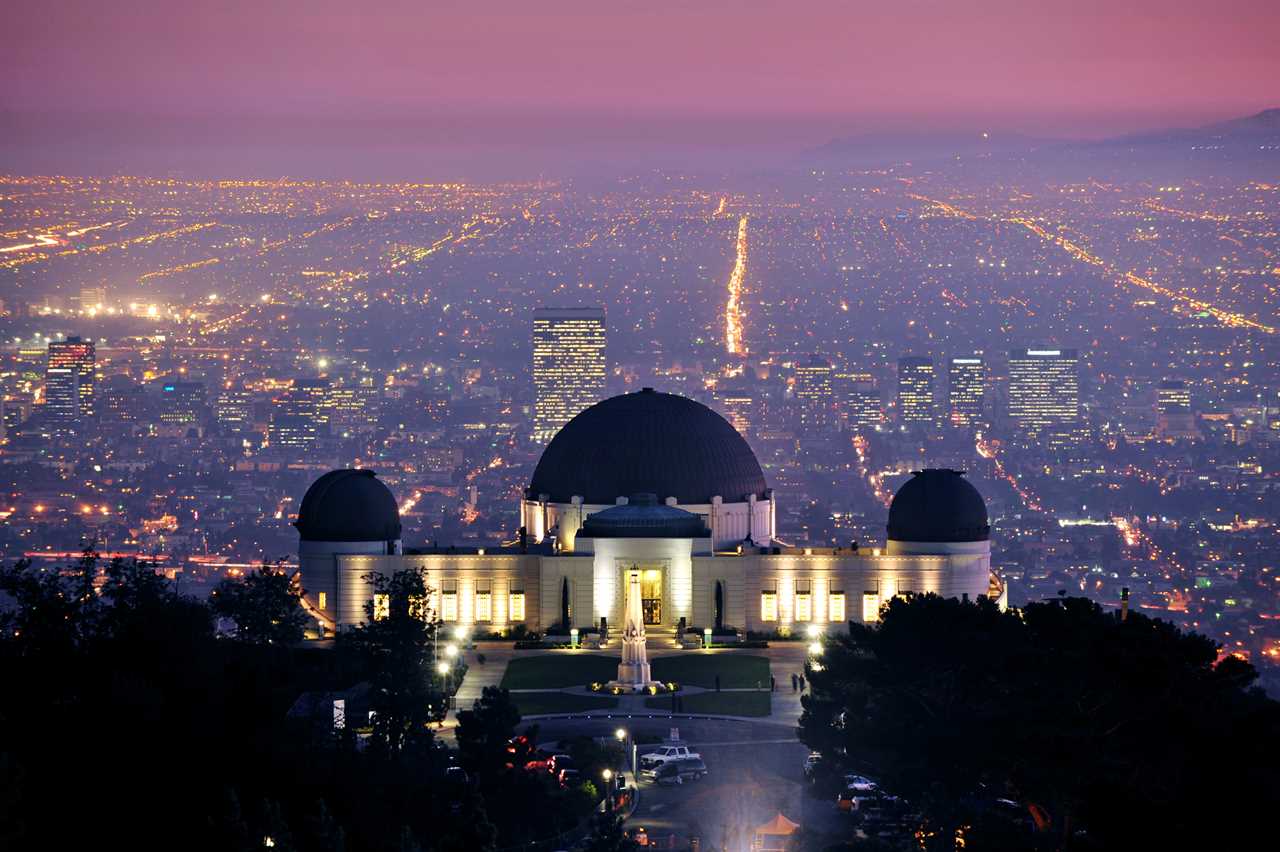 An aerial shot of an observatory overlooking the grid of a metropolis at night.