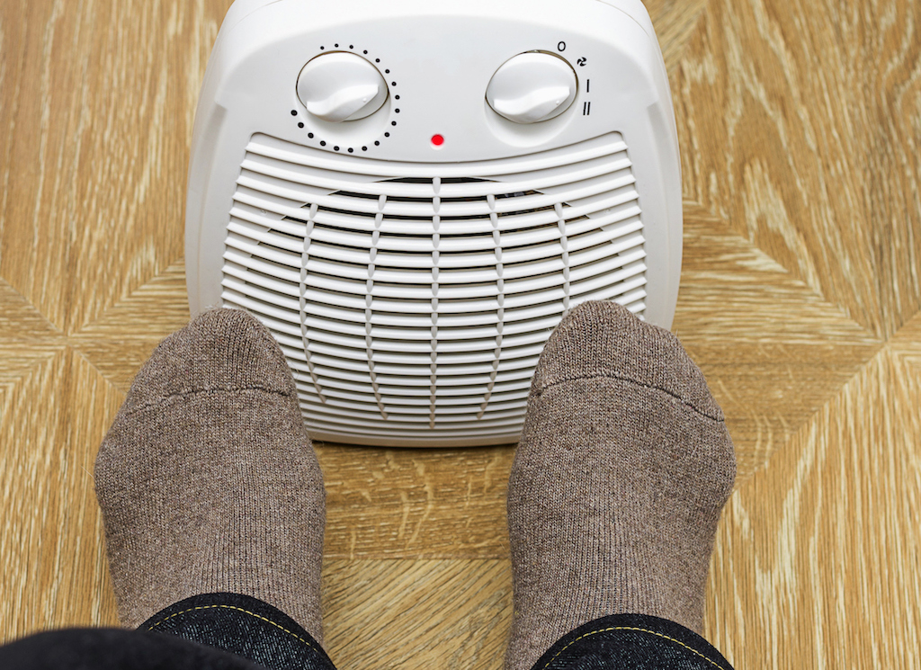 A person warming their feet by an electric space heater