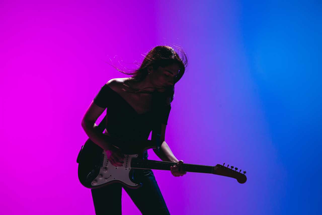 Silhouette of young female guitarist isolated on gradient background in neon.