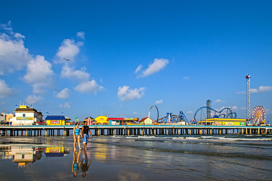 A couple walks on the beach near Galveston's Pleasure Pier.