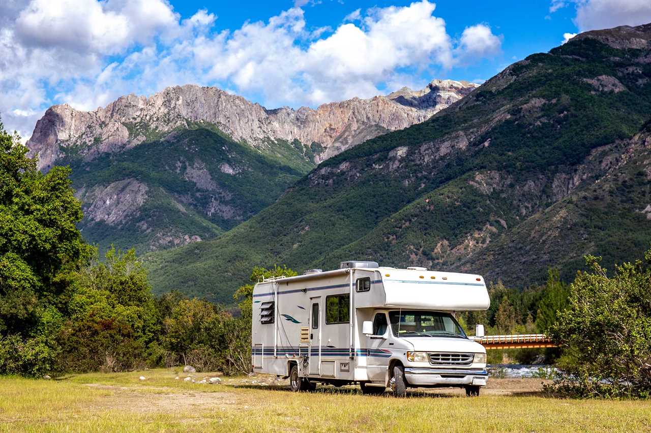 A truck camper parked at a site with towering mountains in background.