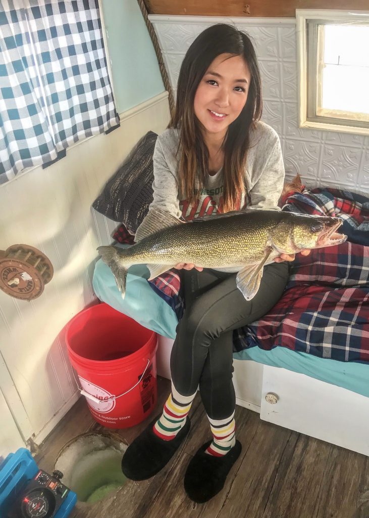 Walleye held over ice hole inside fish house
