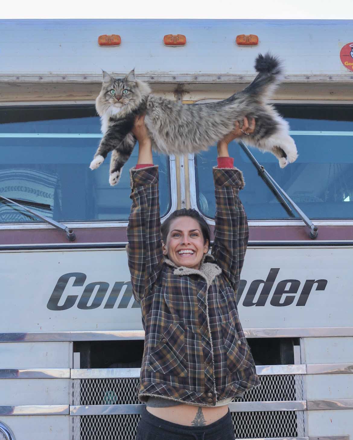 Woman holds a cat over head head in front of motorhome.