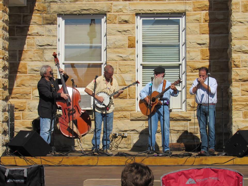 Four men play bluegrass instruments on a stage