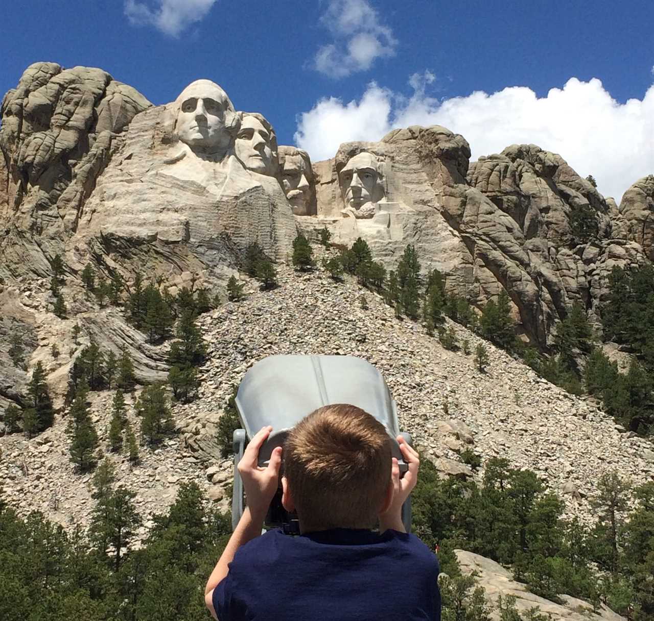 Young man looks at Mount Rushmore through a telescope.