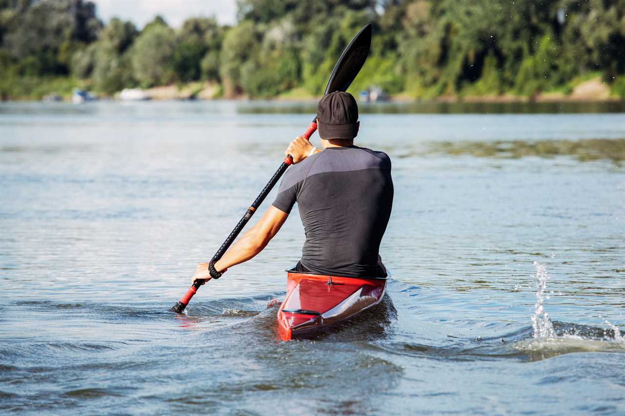 Man paddles a red kayak on a river.