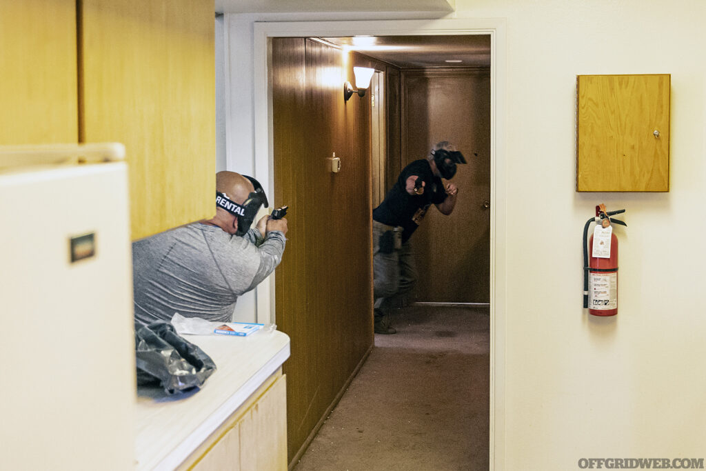 Instructor and student face off on opposite ends of a hallway with airsoft guns during CQB training.
