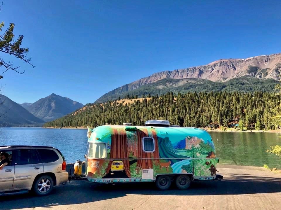 Colorful Airstream trailer parked next to Wallowa Lake with view of mountains 