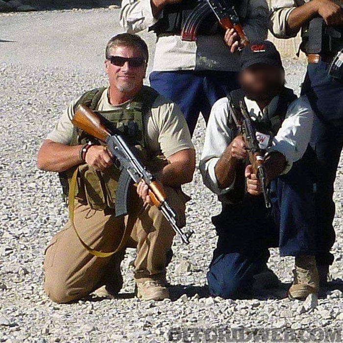 Veteran Timothy Lacy kneels next to another contractor holding an AK.