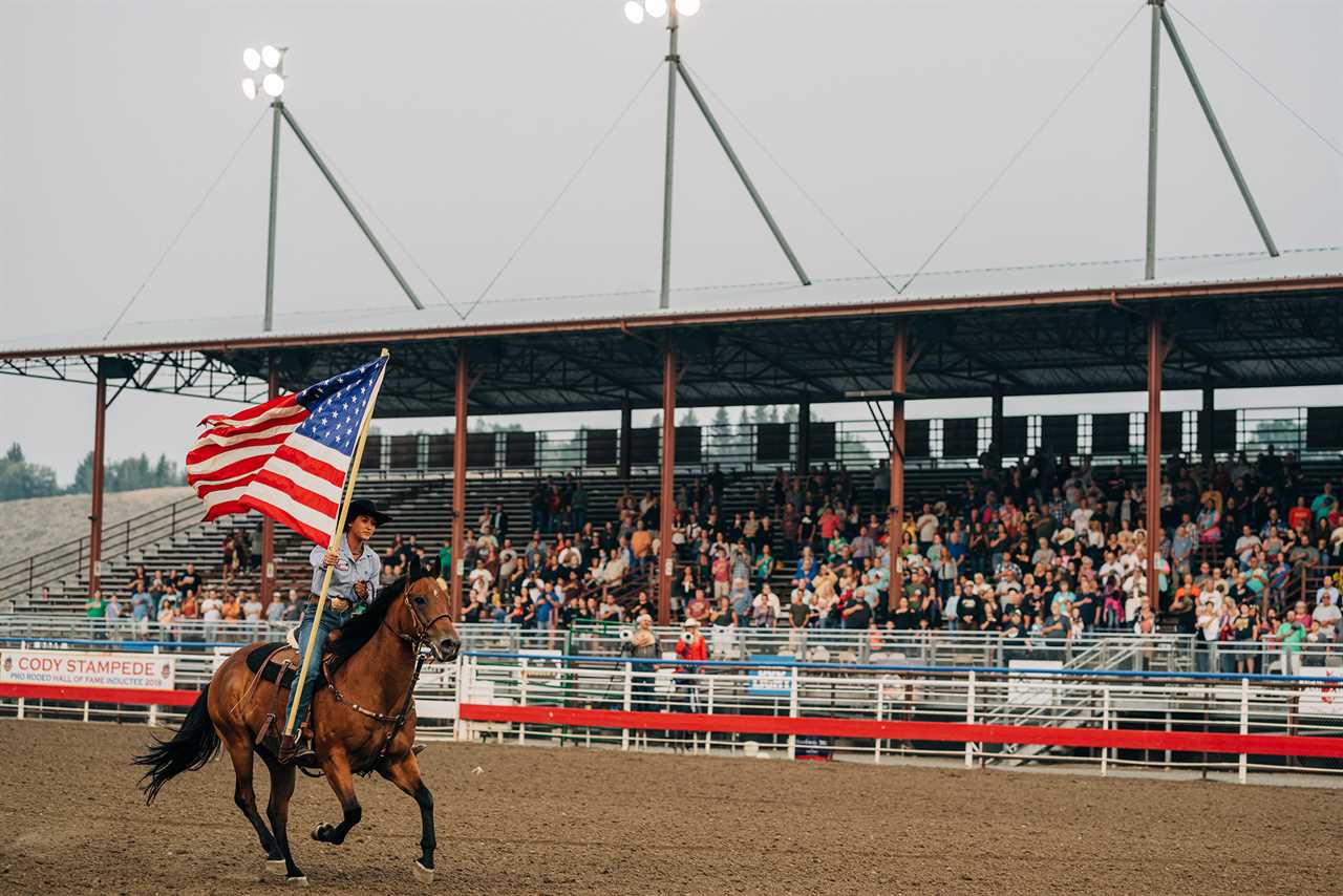 A woman holding an American flag rides in front of bleachers filled with spectators.