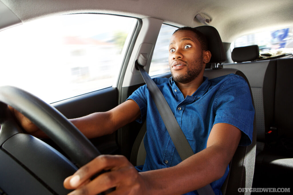 Photo of young man driving a car with surprised expression.