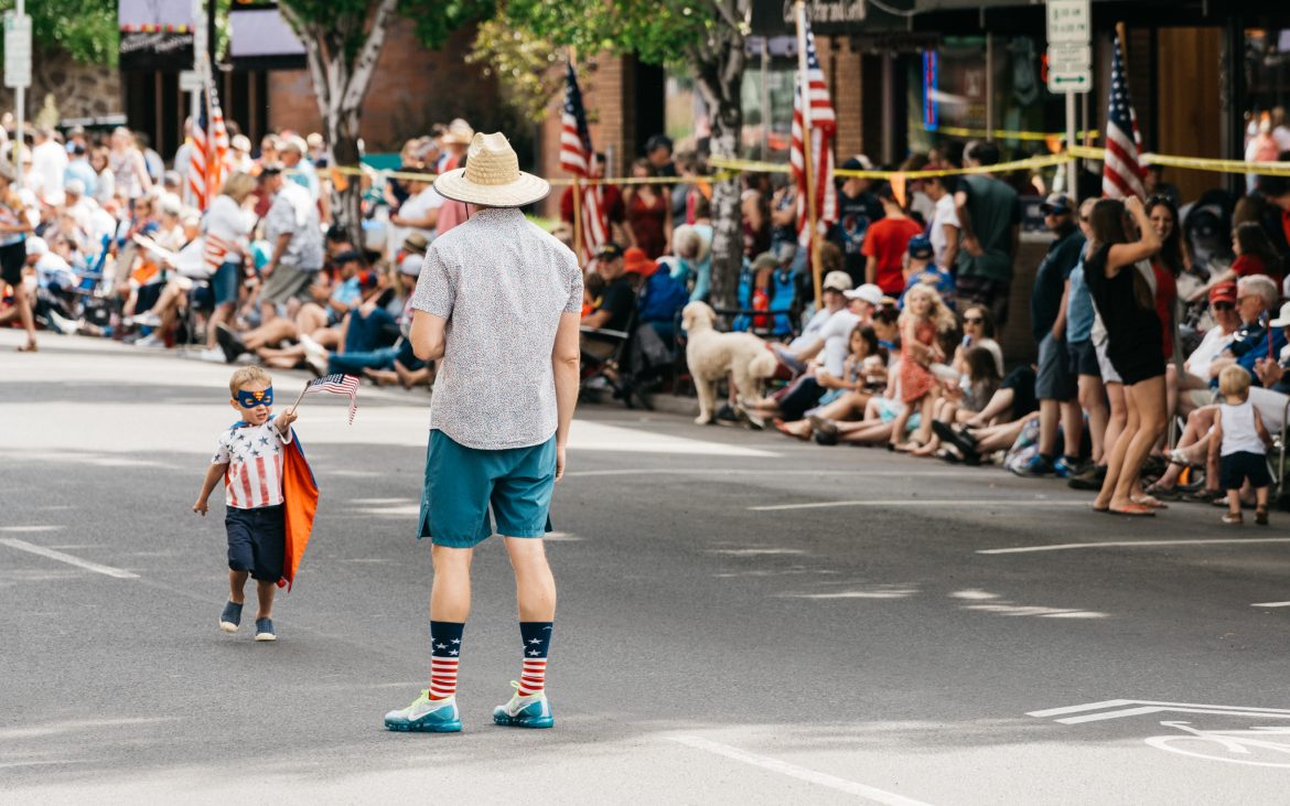 Little boy carrying small American flag with Dad at street parade