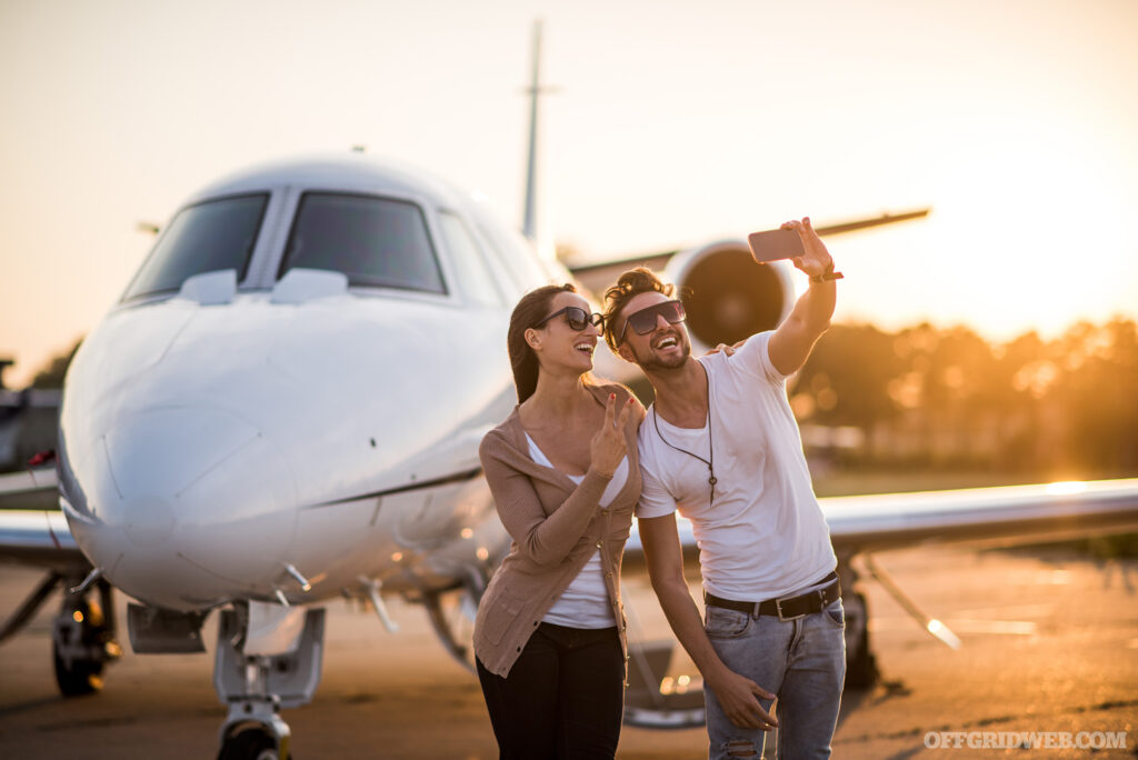 Photo of three young adults in taking a selfie in front of a private jet parked on the tarmac. 