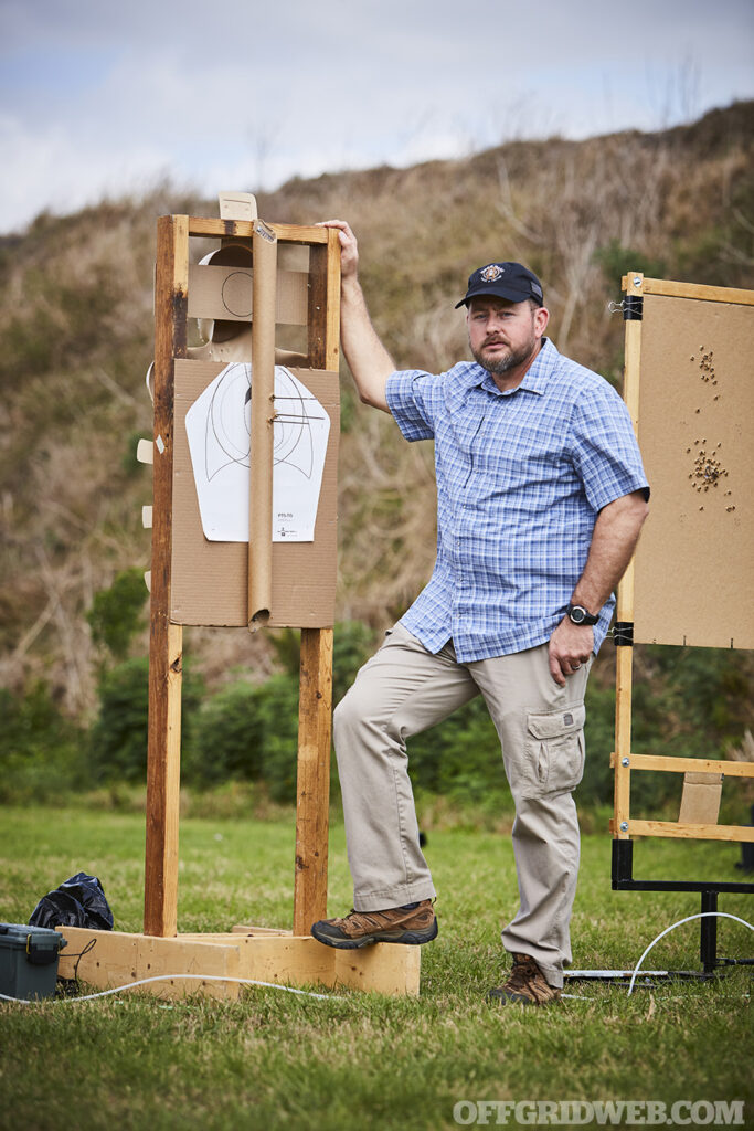 Photo of John Hearne posing in front of a target at a firing range.