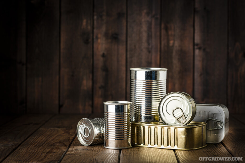 Studio photo of a a pile of unlabeled soup cans, an option for transitional food, stacked on a wooden floor.