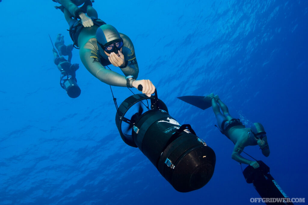 Photo of three survival breathing divers operating sea scooters underwater.