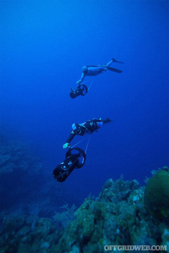 Underwater photo of two freedivers using survival breathing to dive deeper using sea scooters.
