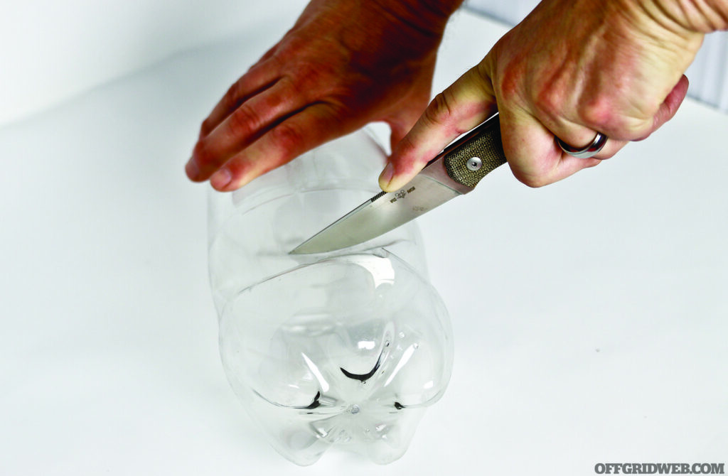 Photo of a someone cutting the conical part off of a clear plastic soda bottle.