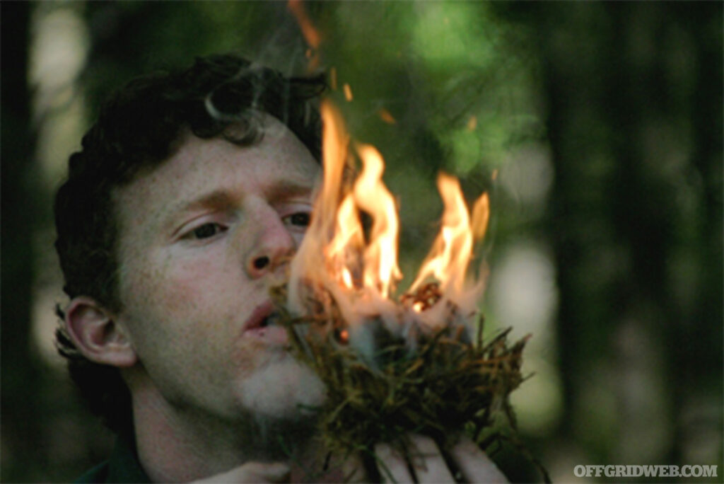 Photo of Frank Grindrod fanning the flames of a tinder bundle.