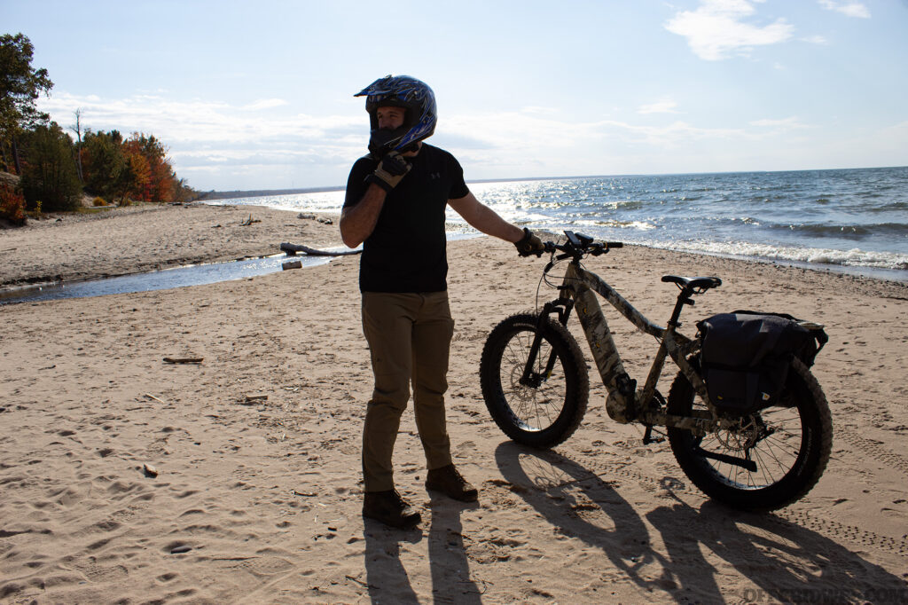 Photo of an adult male getting standing next to a fat-tire eBike on the sandy shores of Lake Superior.