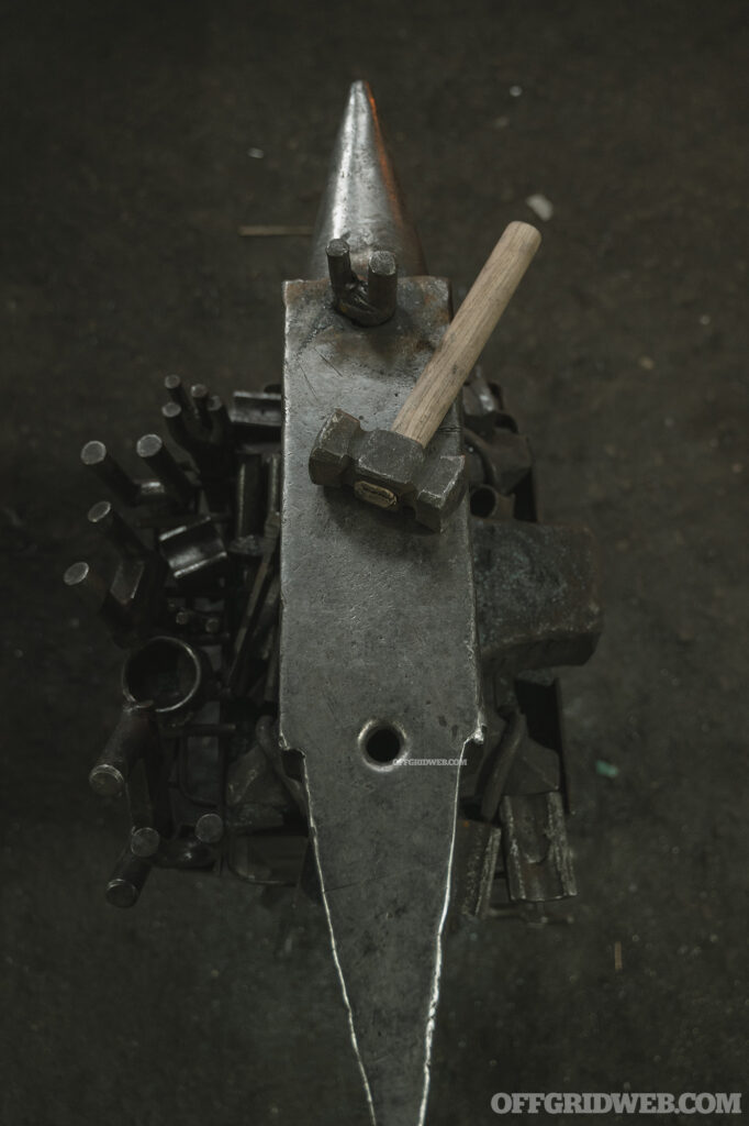 Photo of a hammer resting on the face of a large blacksmithing anvil.