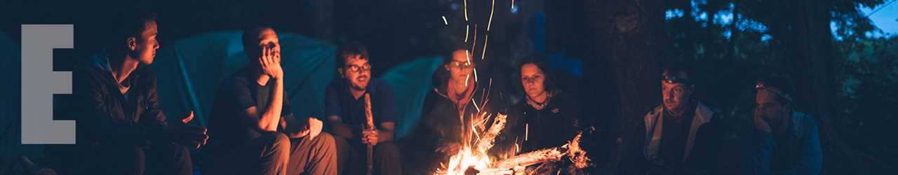 A group gathered around a campfire that throws up sparks.