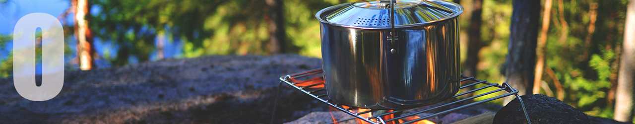 A pot sits on a grill over a campfire in a wooded area.