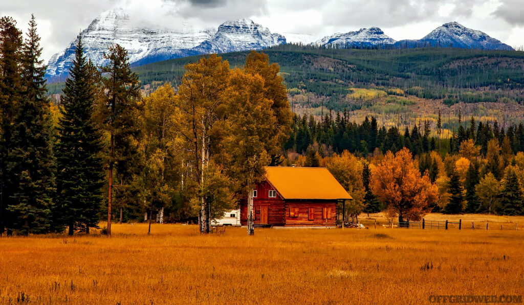 Photo of a truck parked outside of a cabin with mountains in the background.