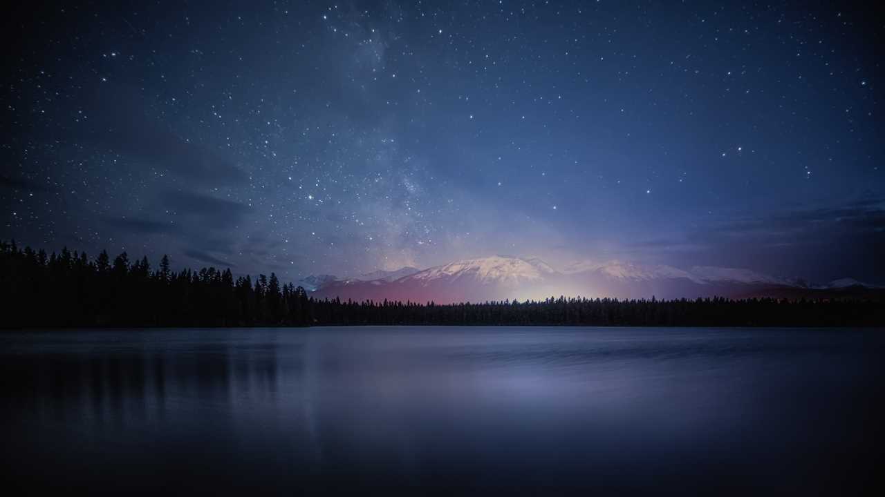 Stars twinkle above a sprawling and calm lake.