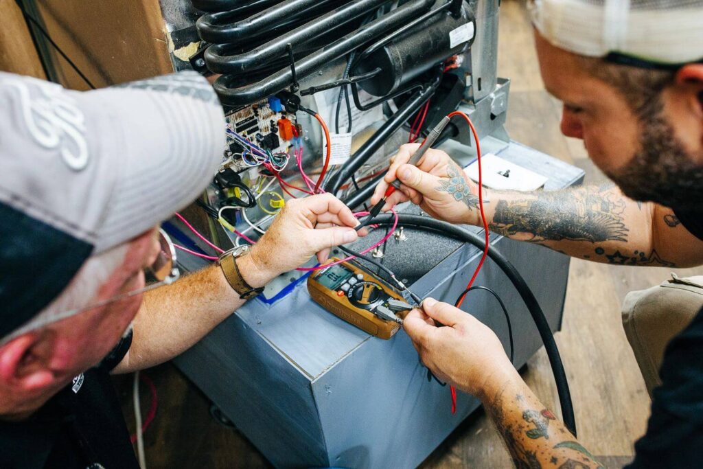 Technicians testing electrical current flow behind RV refrigerator