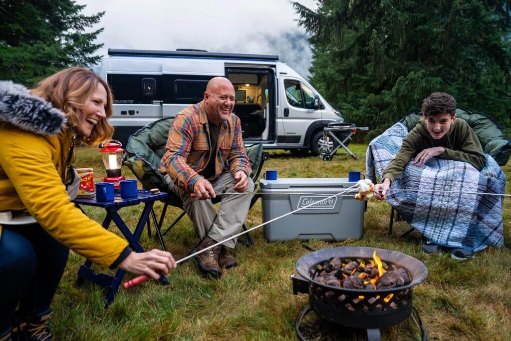 Family roasting marshmallows on portable fire pit outside Class B motorhome