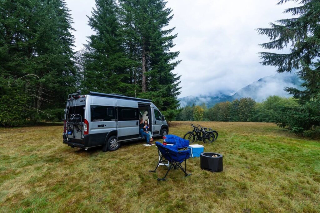 RV Van in open field with grill, cooler, and camping supplies outside